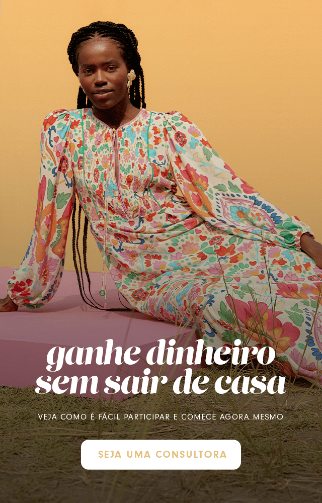  Modelo mulher usando vestido longo estampado colorido com mangas compridas, deitada em um campo de grama. Banner indica: ganhe dinheiro sem sair de casa. Seja uma consultora!